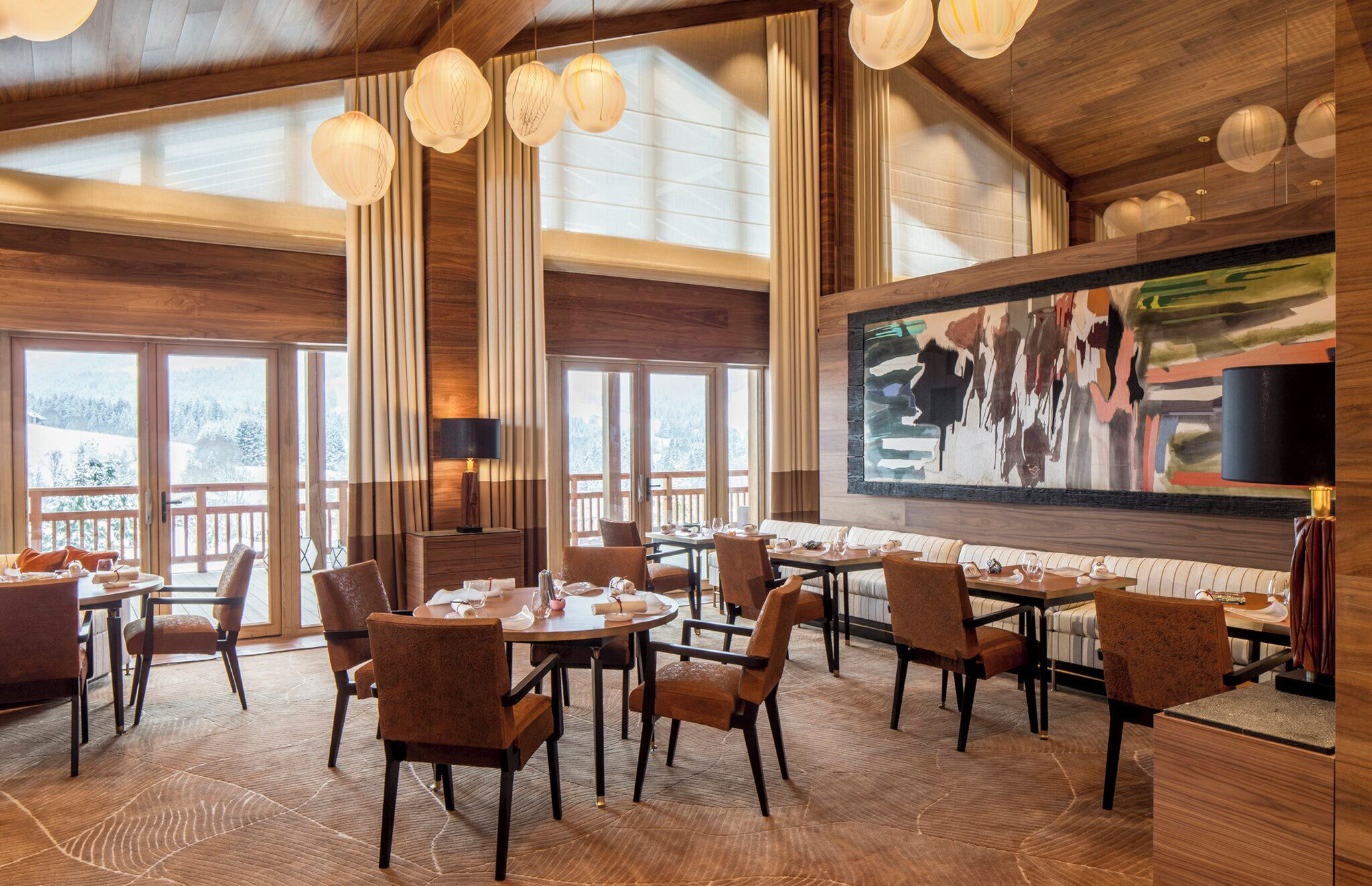A spacious dining area with high ceilings and large windows, featuring wooden furniture and a modern art piece on the wall.