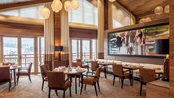 A spacious dining area with high ceilings and large windows, featuring wooden furniture and a modern art piece on the wall.