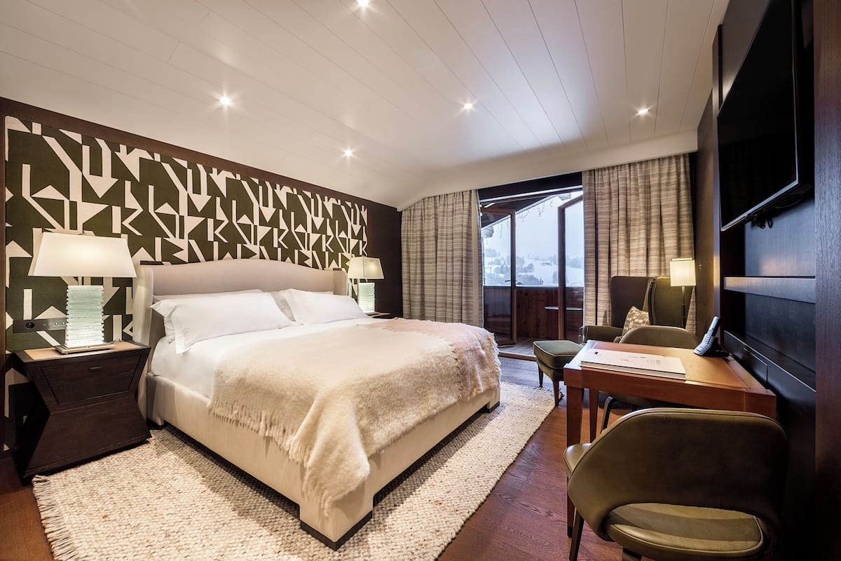 A modern hotel room with a large bed, a desk with a chair, a flat-screen TV, and a view of the outdoors.