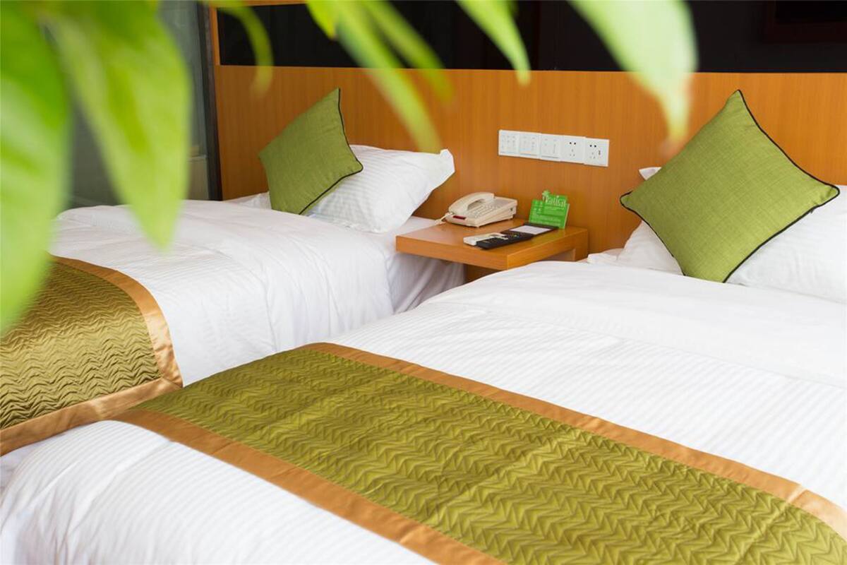 A hotel room with two beds, each with white bedding and green pillows. There is a wooden nightstand with a telephone and a green tray table.