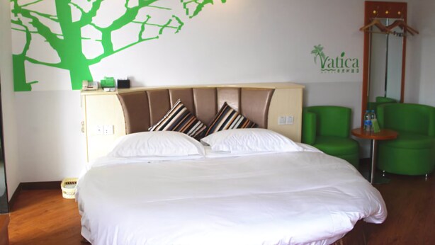 Ein Hotelzimmer mit einem Bett, einem Kopfteil, einem grünen Stuhl, einem kleinen Tisch und einer Wand mit einer Baumaufkleber.