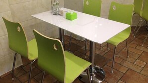 Ein Essbereich mit einem weißen Tisch und grünen Stühlen. Auf dem Tisch steht eine Vase mit einer Rose und eine grüne Schachtel.