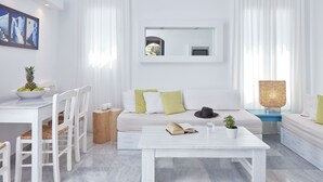 A modern living room with a white sofa, a dining table with chairs, a coffee table, and a side table with a lamp. - Mykonos Town Suites (Mykonos)
