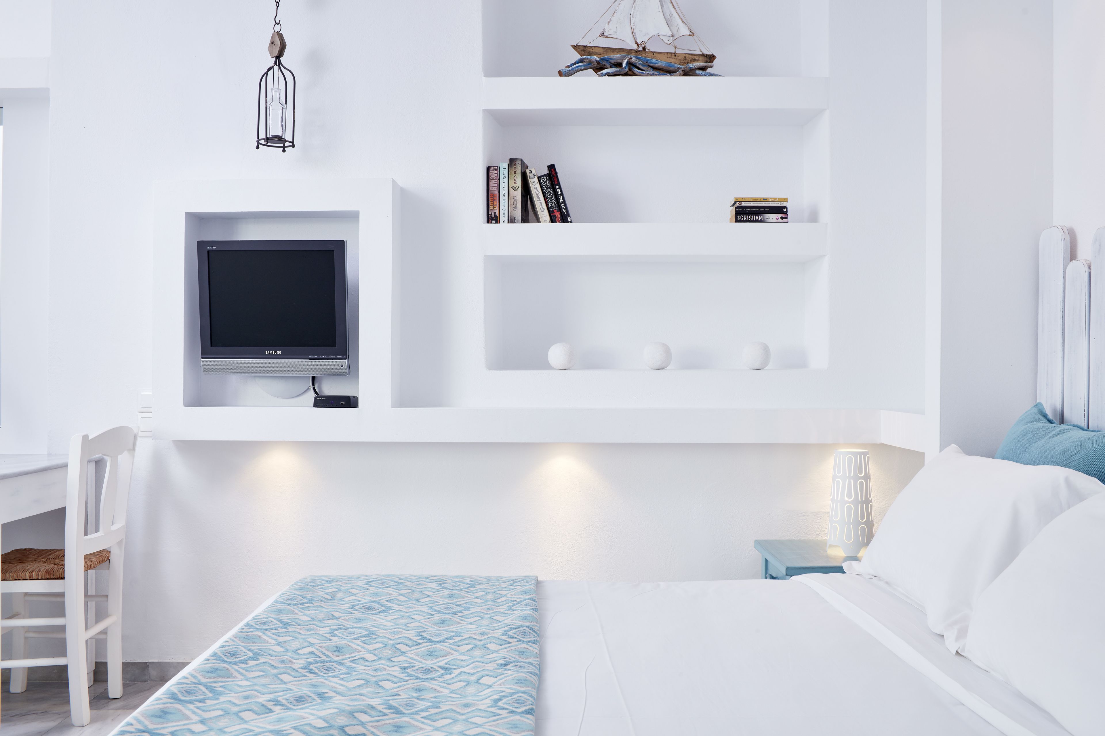 Quarto moderno com cama, televisão, estante e mesa de cabeceira.