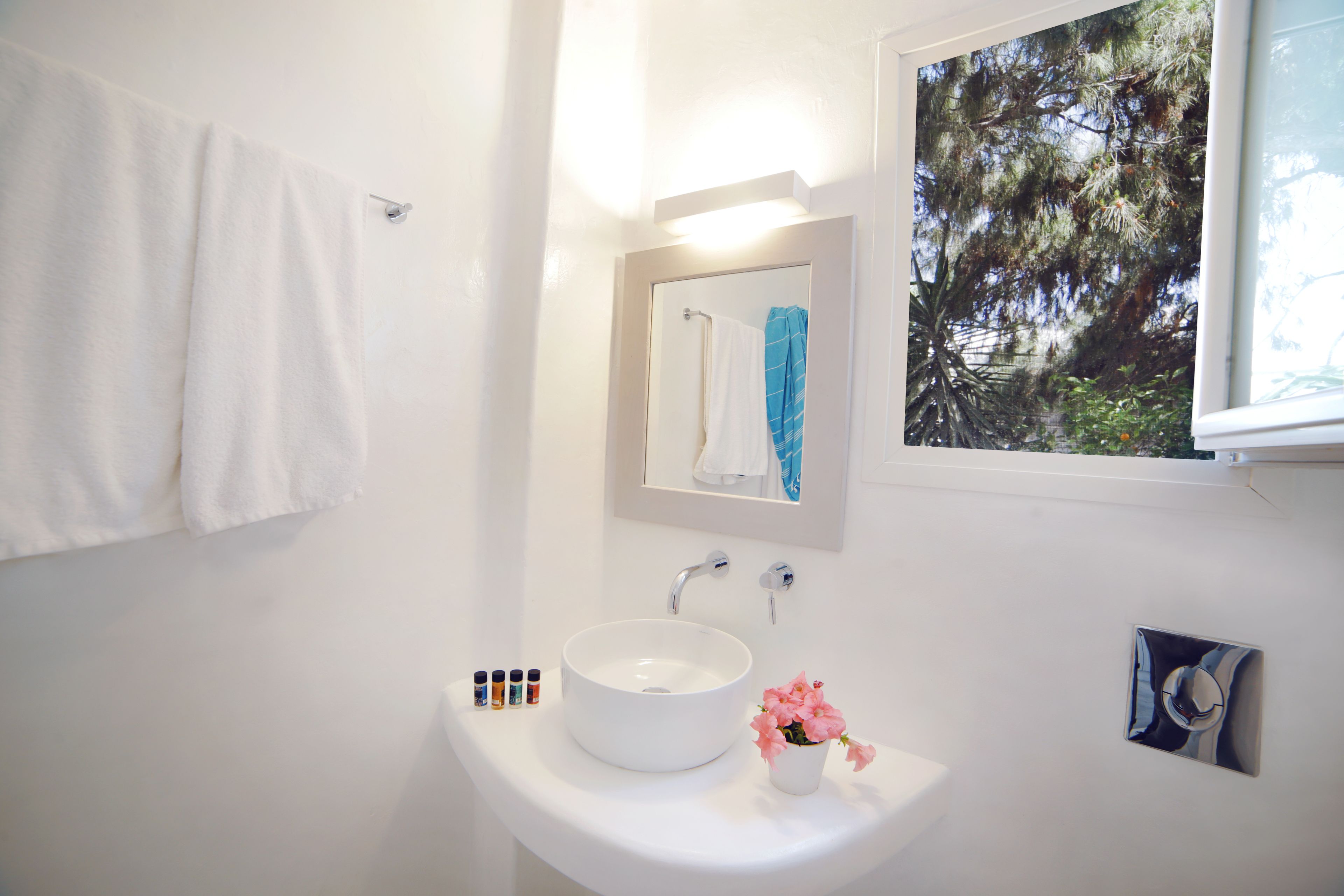 A bathroom with a white sink, a mirror, and a window with a view of trees.