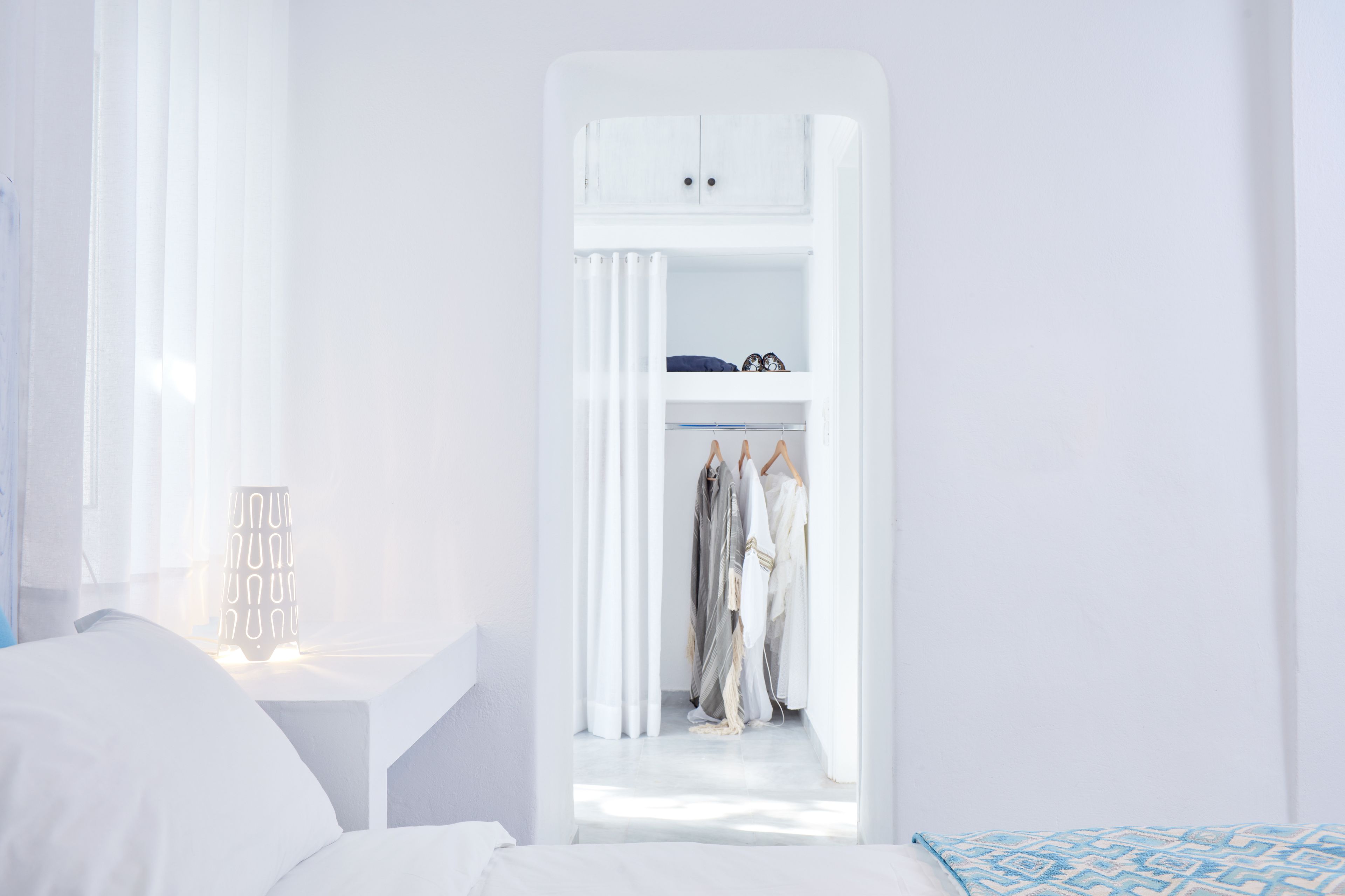 A bedroom with a bed, a bedside table with a lamp, and a closet with hanging clothes.