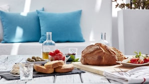 A dining table with bread, cheese, olives, and a bottle of olive oil. - Mykonos Town Suites (Mykonos)