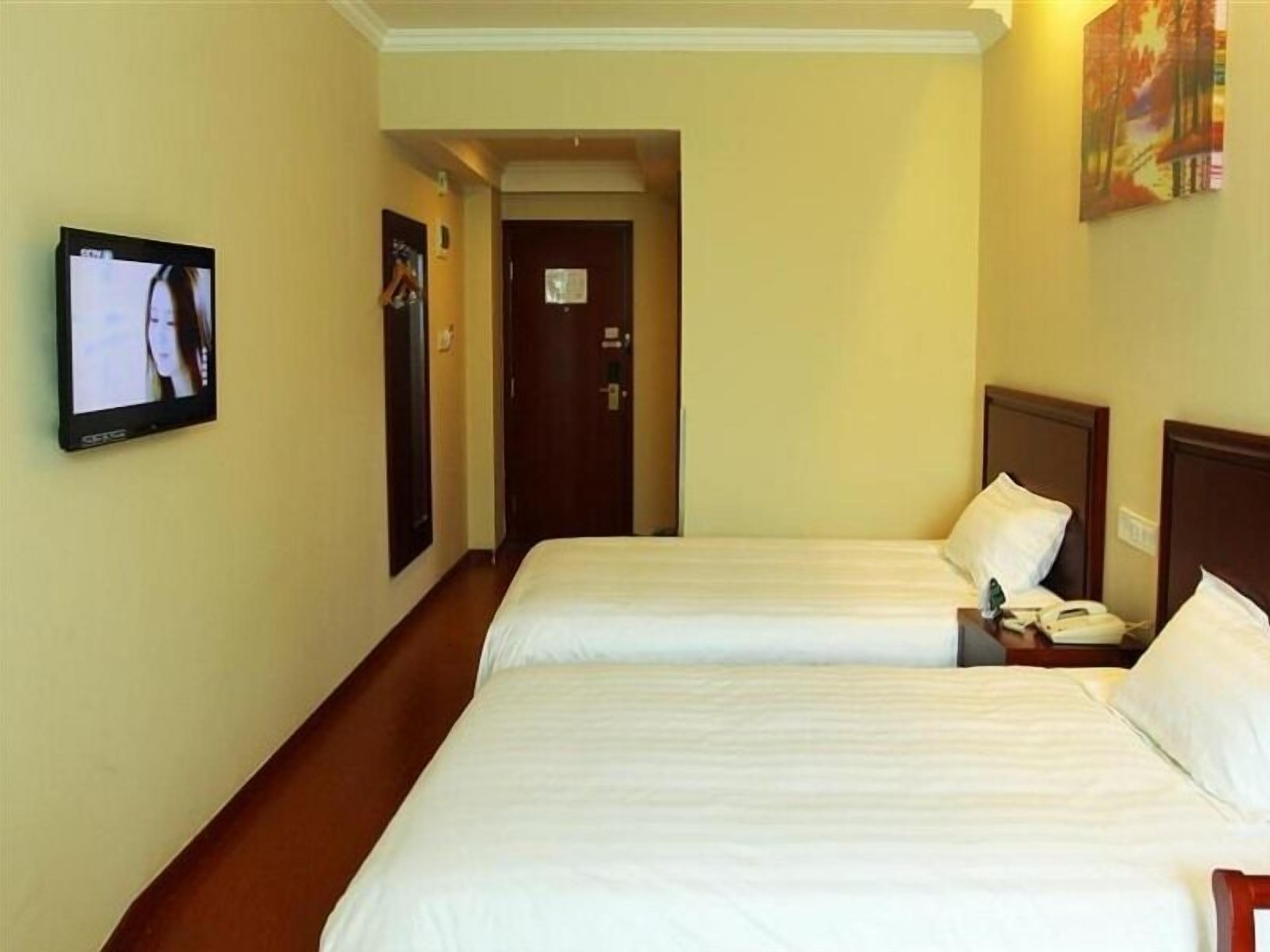 A hotel room with two beds, a television on the wall, and a door leading to another room.