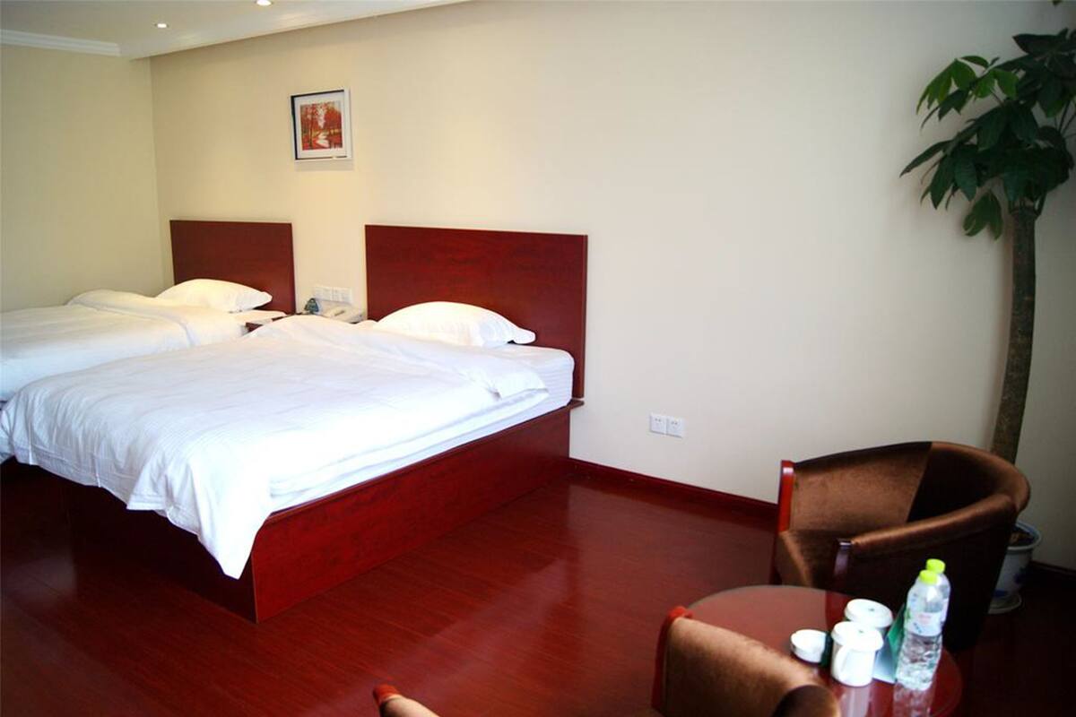 A hotel room with two beds, a wooden headboard, a small table with a chair, and a potted plant.