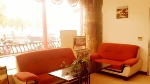 A living room with a red sofa, a coffee table, and a large window with curtains. - GreenTree Inn Yangzhou Jiangdu West Changjiang Road Liberty Park Business Hotel (Yangzhou)