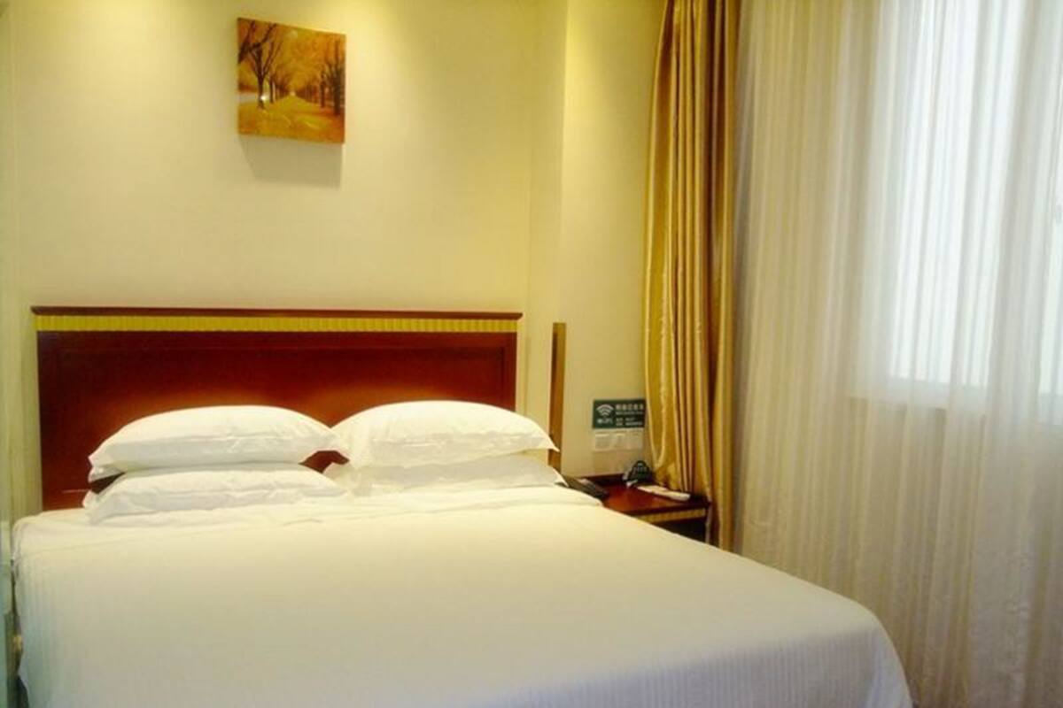A hotel room with a large bed, a wooden headboard, a nightstand with a phone and a sign, and a painting on the wall.