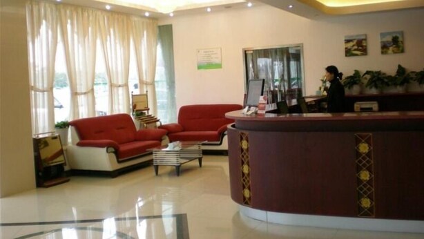 A hotel lobby with a reception desk, two red sofas, a coffee table, and a large window with curtains. - GreenTree Inn Yangzhou Jiangdu West Changjiang Road Liberty Park Business Hotel (Yangzhou)