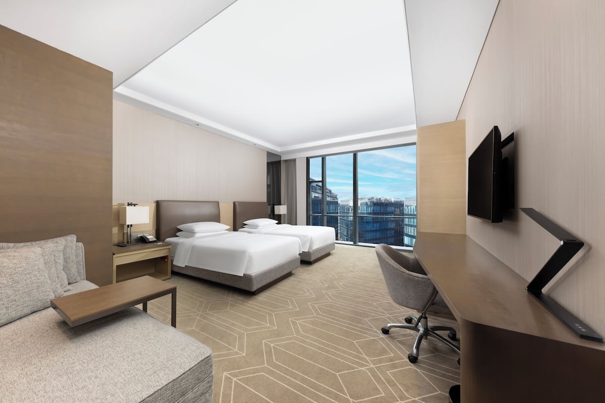 Une chambre d’hôtel avec deux lits, un bureau, une télévision et une grande fenêtre donnant sur la ville.