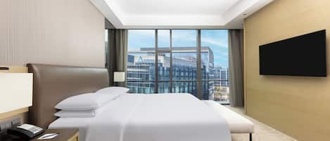 Une chambre d’hôtel avec un grand lit, un bureau avec un téléphone, un téléviseur fixé au mur et une vue sur un immeuble orné du logo Delta.