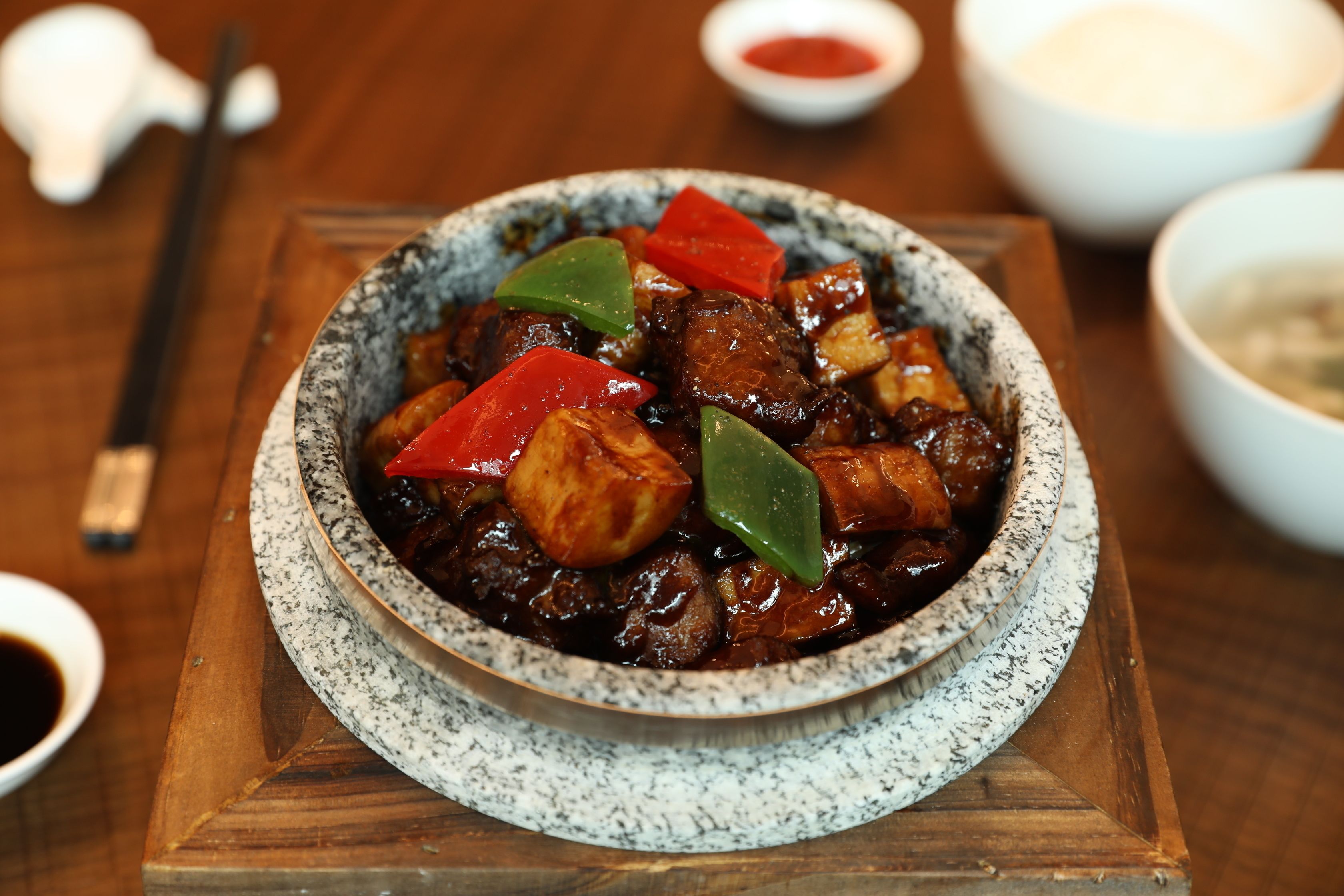 A bowl of food with red and green bell peppers, meat, and sauce, served on a speckled ceramic plate.