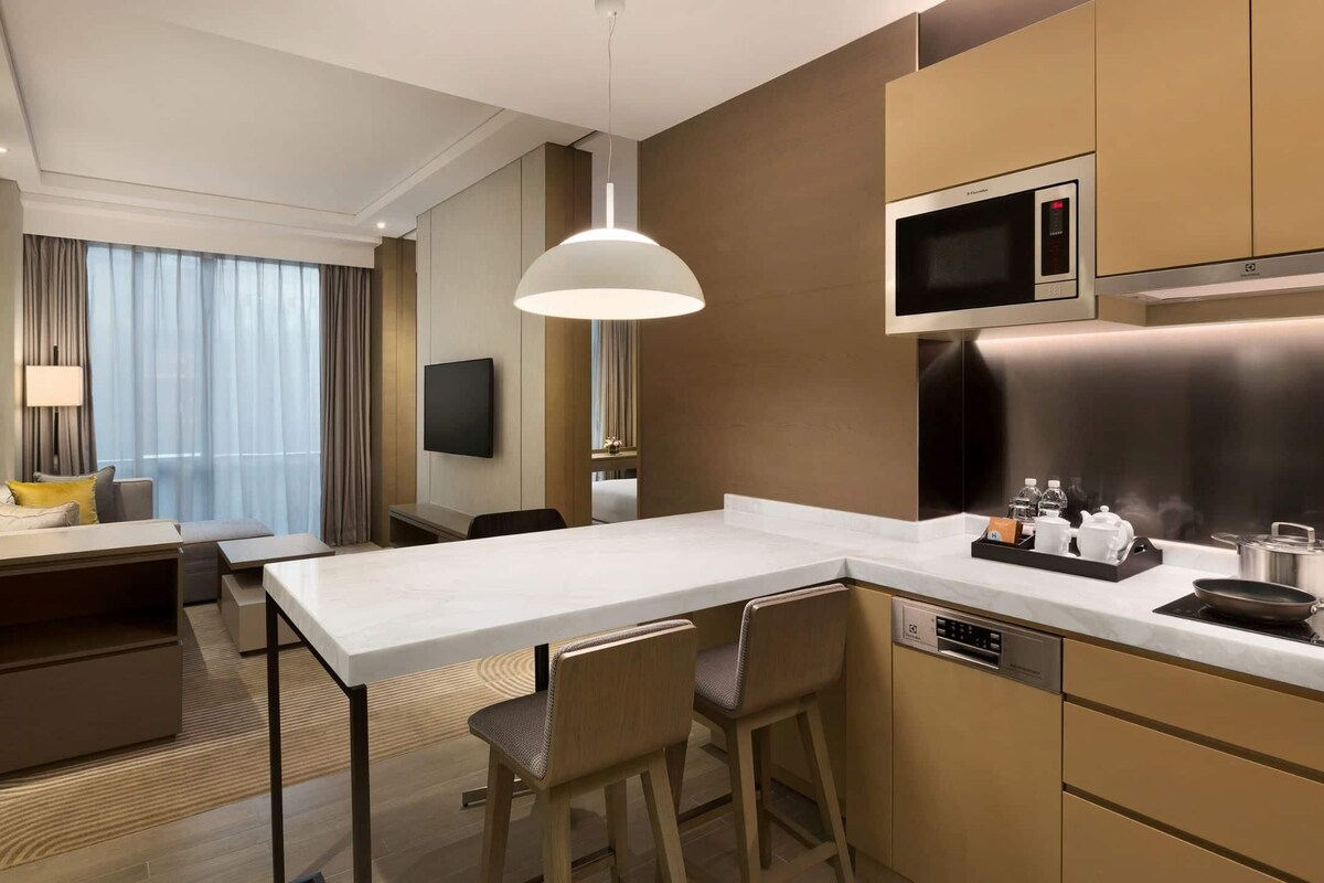 Une chambre d’hôtel moderne dotée d’une kitchenette, d’un coin repas et d’un téléviseur fixé au mur.