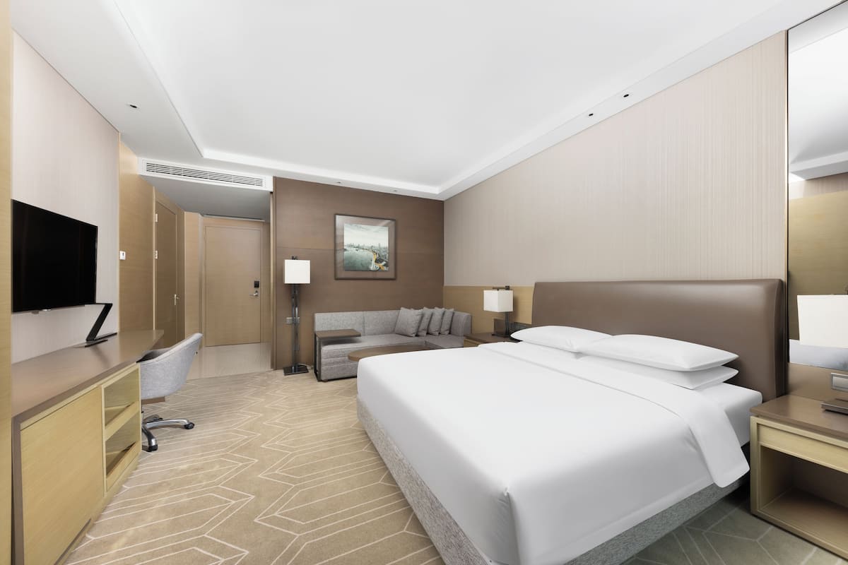 Une chambre d’hôtel avec un grand lit, un bureau avec une chaise, un canapé et un téléviseur fixé au mur.