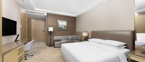 Una habitación de hotel con una cama grande, un escritorio con una silla, un sofá y un televisor en la pared.