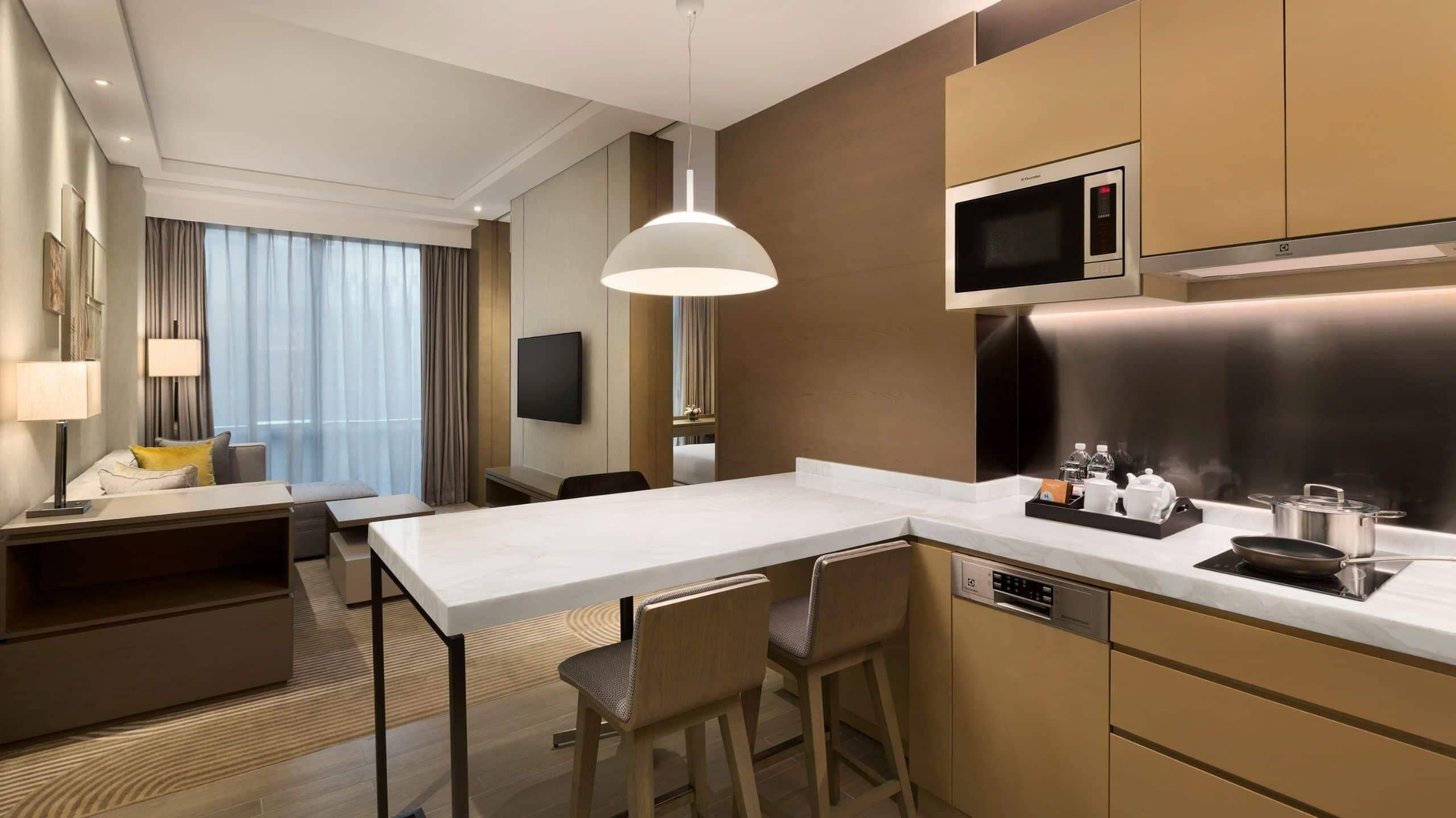 Habitación de hotel moderna con kitchenette, zona de comedor y televisor montado en la pared.