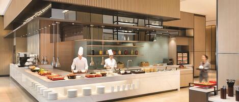 A modern kitchen with chefs preparing food, a buffet setup with various dishes, and a clean, contemporary design.