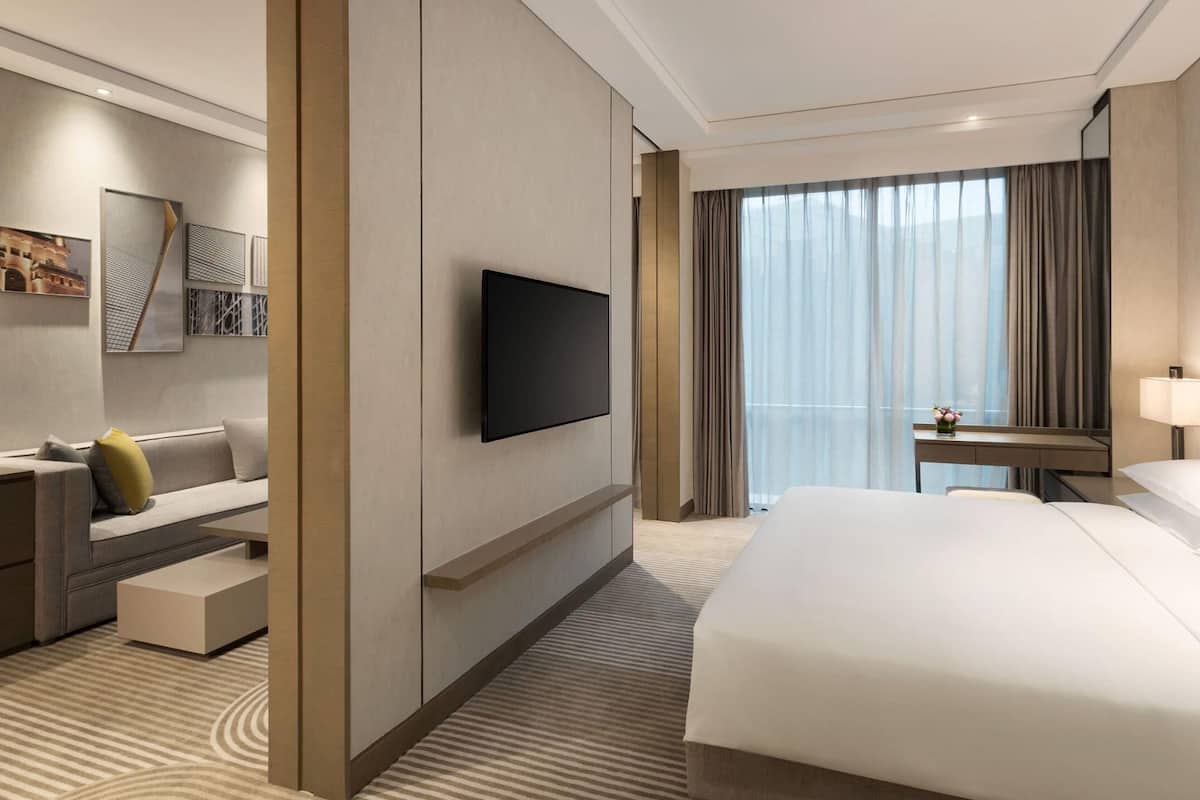 Une chambre d’hôtel moderne dotée d’un grand lit, d’un téléviseur à écran plat fixé au mur, d’un bureau avec une chaise et d’une petite table avec une lampe.