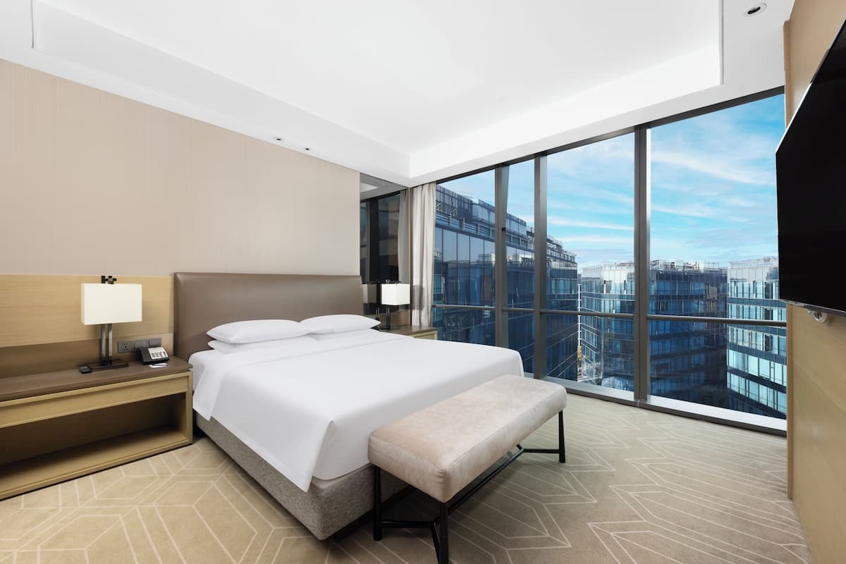 Une chambre d’hôtel moderne avec un grand lit, une banquette, une table de chevet, une lampe et un téléviseur.