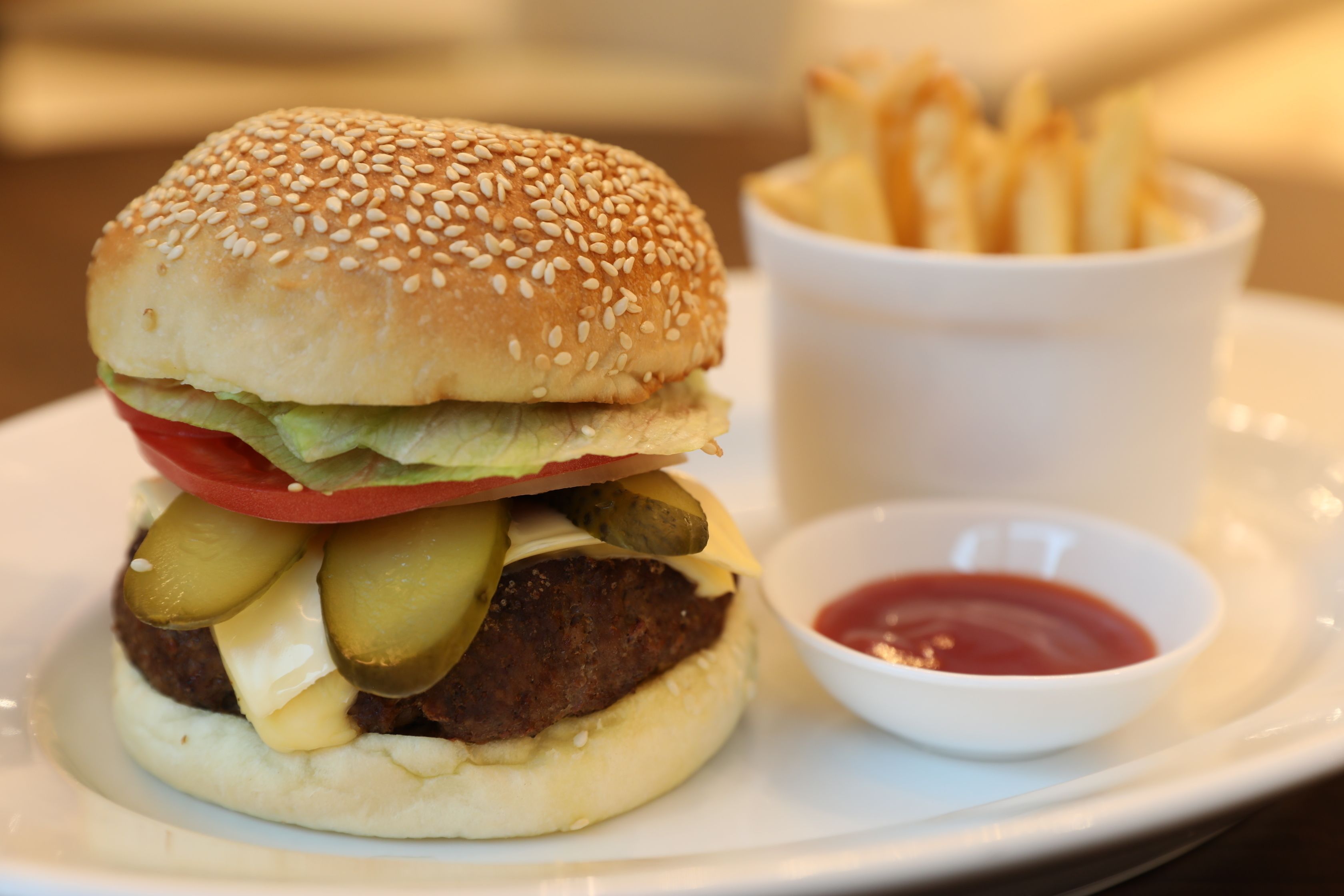 A hamburger with pickles, cheese, and a sesame seed bun, served with fries and ketchup.