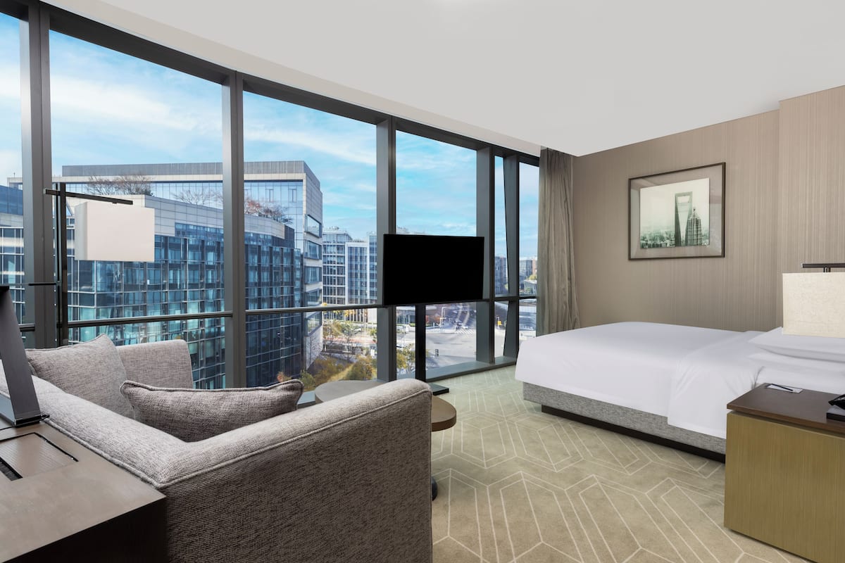Une chambre d’hôtel avec une grande fenêtre, un lit, un bureau et une chaise.