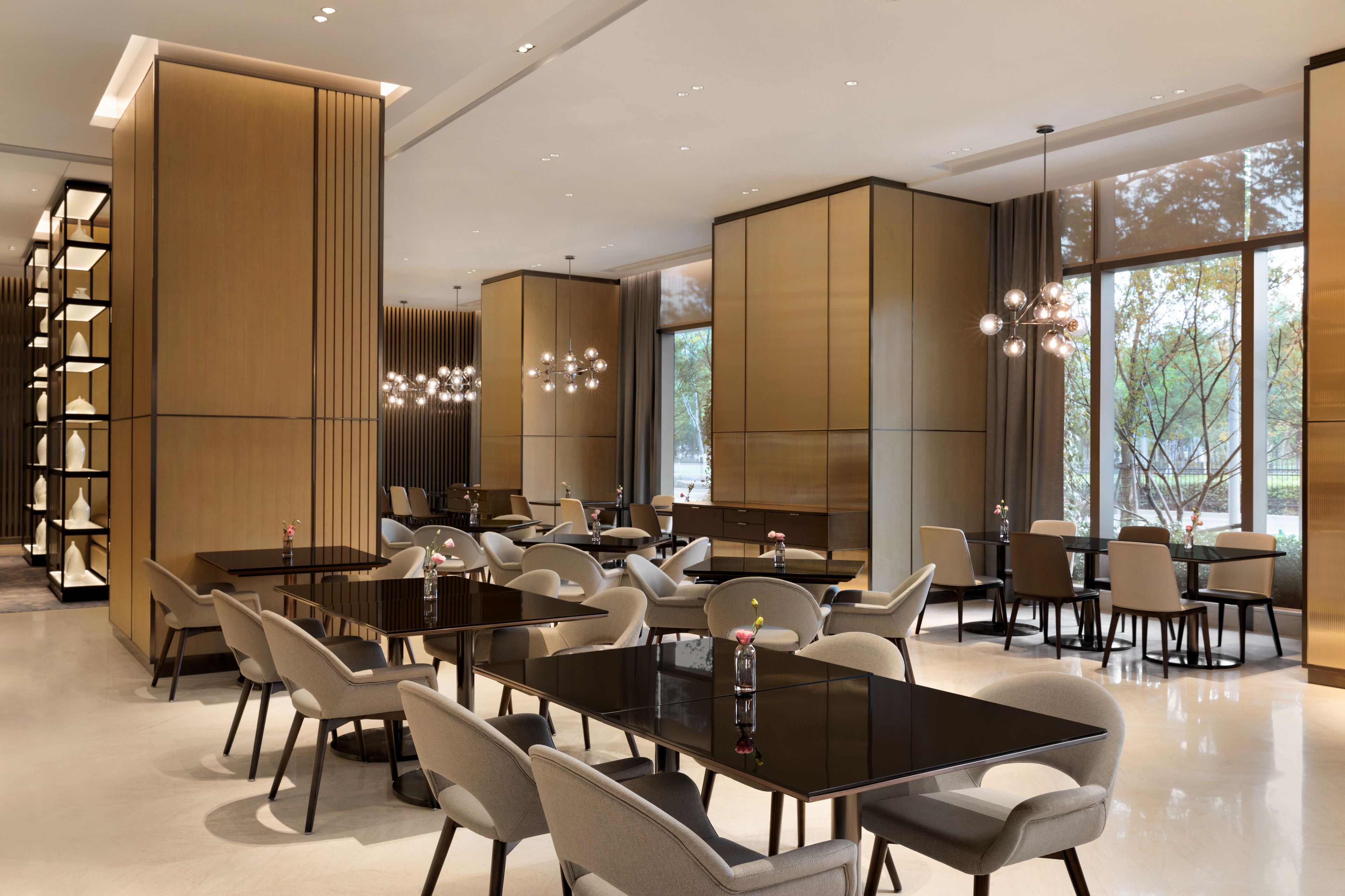 A modern dining area with multiple tables and chairs, large windows, and a decorative light fixture.