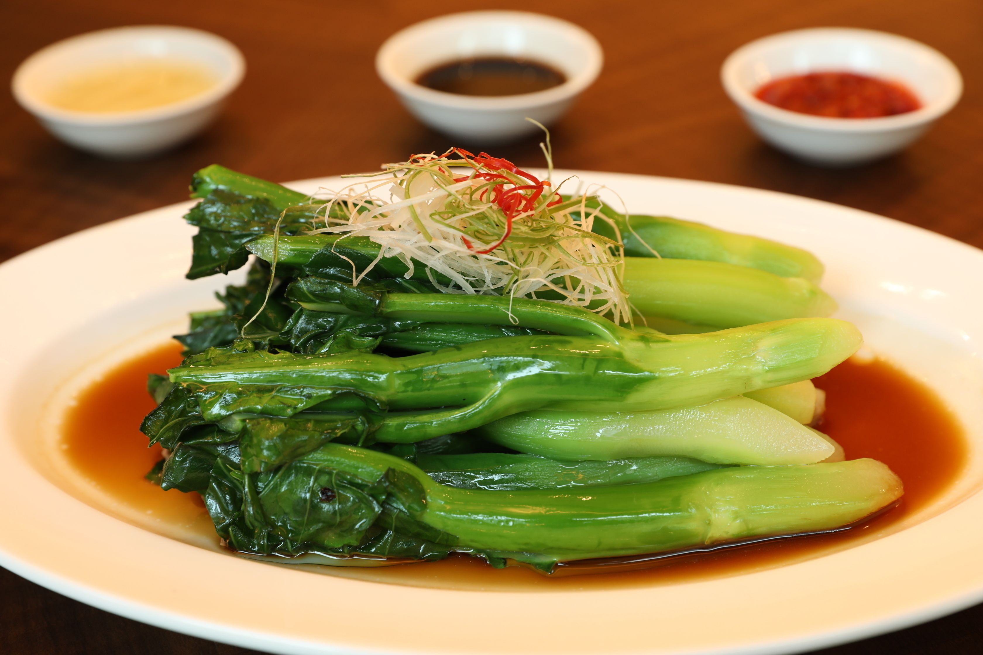 A plate of bok choy with a light dressing and three small bowls of dipping sauces.