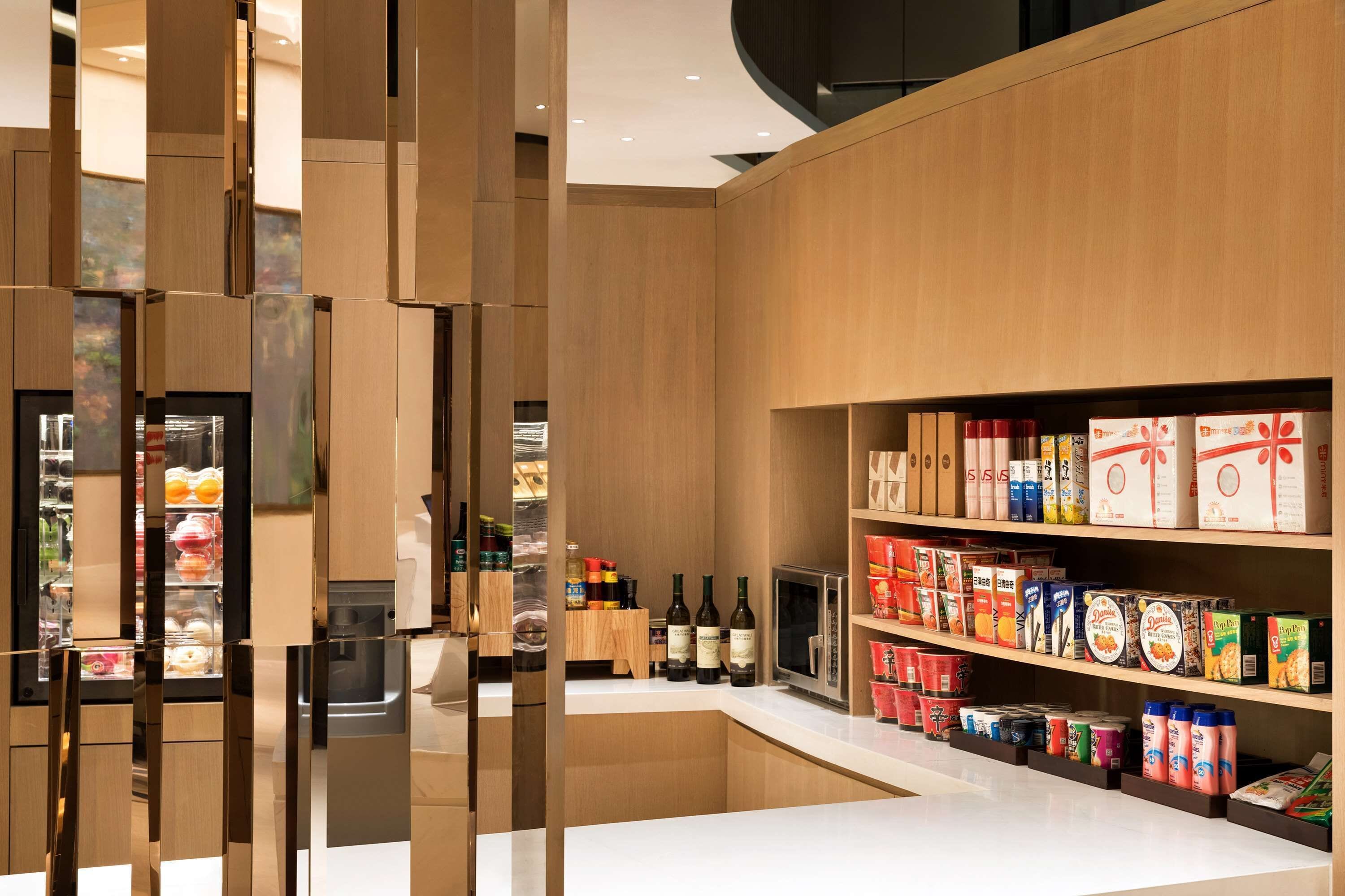 A modern kitchen with wooden cabinetry, a built-in refrigerator, and a variety of food items and beverages on shelves.