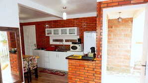 A compact kitchen with a brick wall, white cabinets, a microwave, and a refrigerator. - Apartamento Vista do Centro Gramado 02 (Gramado)