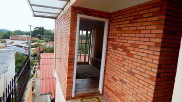 A balcony with a red brick wall, a glass door leading to an interior space, and a tiled floor with a doormat.
