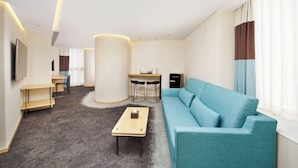 A modern living room with a blue sofa, a coffee table, a TV, a desk, and a chair. - Hotel 108 (Kowloon)