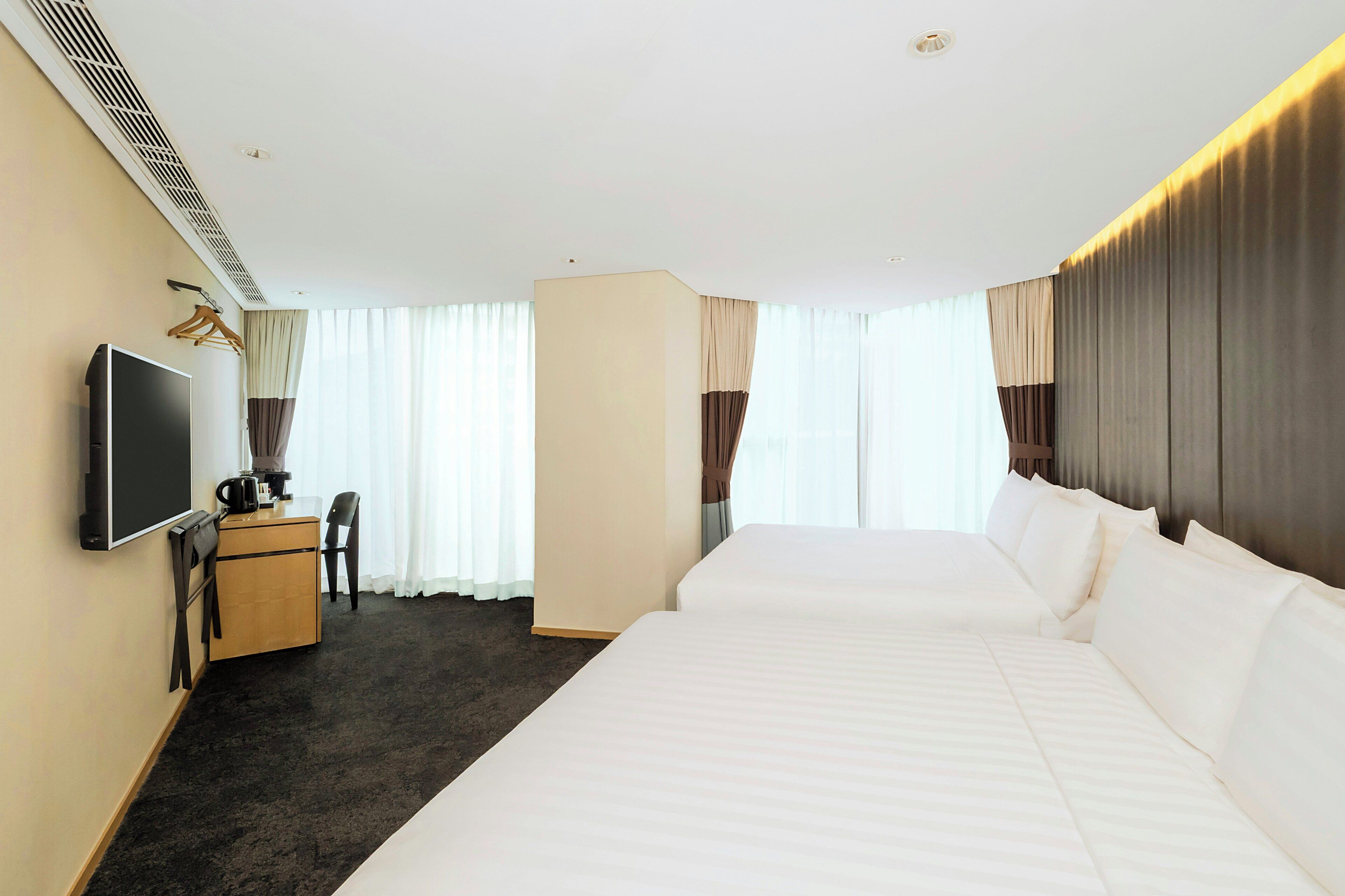 A hotel room with a large bed, a desk with a chair, a television, and a wardrobe.