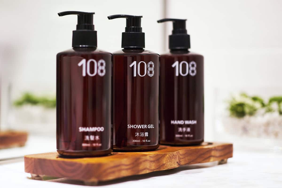 Three bottles of shower gel and shampoo on a wooden tray.
