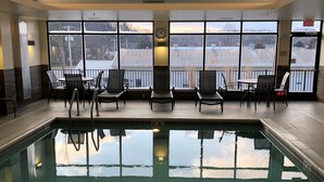 Une piscine intérieure avec de grandes fenêtres, des chaises et une horloge.