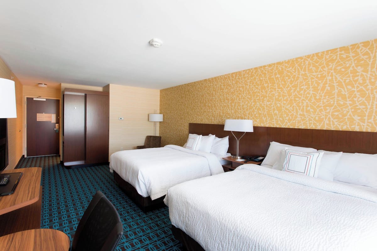 A hotel room with two beds, a desk, and a chair.