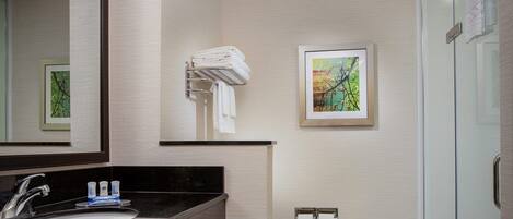A modern bathroom with a black countertop sink, a large mirror, a framed painting, and a glass shower enclosure.