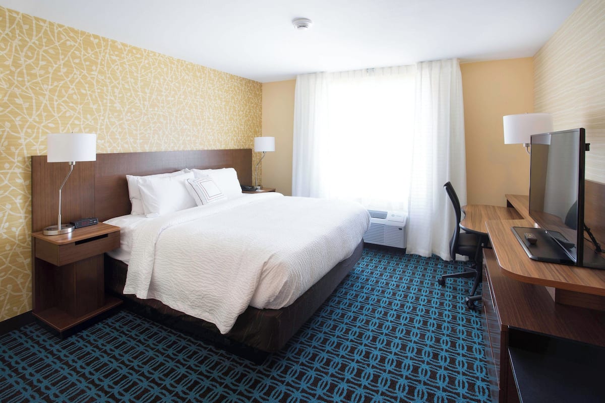 A hotel room with a bed, bedside lamps, a desk with a computer, and a large window with curtains.