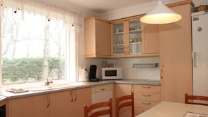 A kitchen with wooden cabinets, a microwave, a coffee maker, and a window with curtains. - Olga Guesthouse (Egilsstaðir)