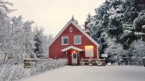A red guesthouse with a white door and windows, surrounded by snow-covered trees and bushes. - Olga Guesthouse (Egilsstaðir)