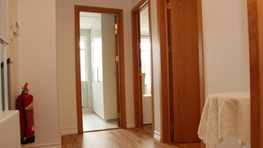 A hallway with wooden flooring, a fire extinguisher, and a table with a white tablecloth. - Olga Guesthouse (Egilsstaðir)