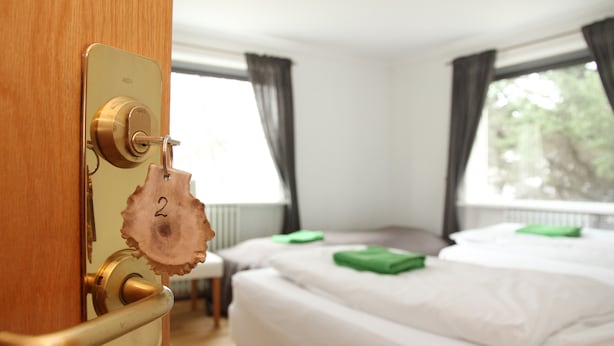 A hotel room with a wooden door, a keyhole, a bed with white bedding, and a window with curtains. - Olga Guesthouse (Egilsstaðir)