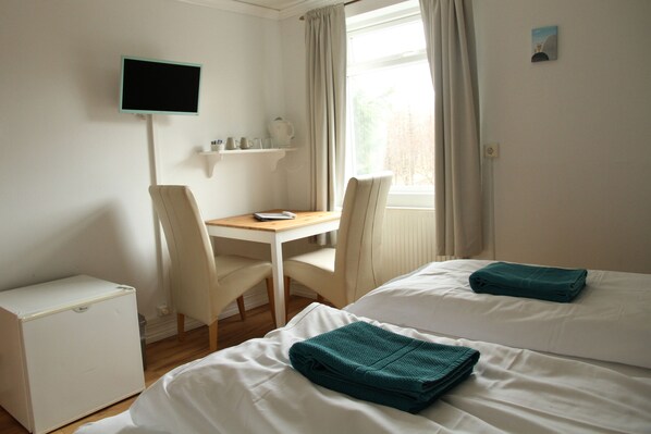 A hotel room with two beds, a desk with a chair, a television, and a small shelf with items.