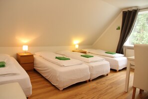 Una habitación con cuatro camas individuales, suelo de madera y ventana con cortinas.