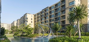 Un immeuble résidentiel moderne doté de nombreux balcons et d’une piscine agrémentée d’une sculpture métallique décorative.