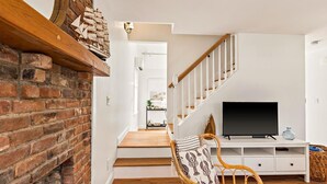 A staircase leading to a second floor with a white wall, a TV on a white stand, and a wicker chair with a patterned cushion. - Walk To Town - Beautiful Edgartown House  (Edgartown)