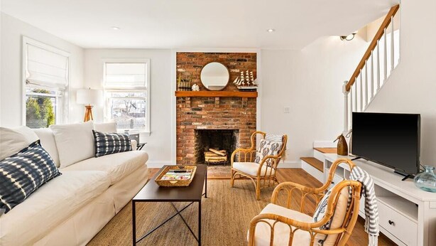 A living room with a brick fireplace, white sofa, wicker chairs, and a TV on a white stand. - Walk To Town - Beautiful Edgartown House  (Edgartown)