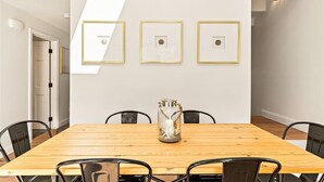 A dining area with a wooden table, black chairs, and a glass jar centerpiece. Three framed pictures are hung on the wall above the table. - Walk To Town - Beautiful Edgartown House  (Edgartown)
